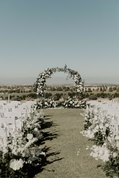 an outdoor ceremony setup with white flowers and greenery on the aisle, surrounded by chairs