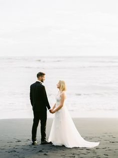 a bride and groom holding hands on the beach