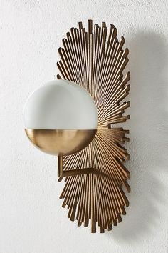 a gold and white wall light mounted to the side of a wall next to a mirror