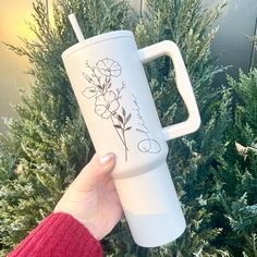 a person holding up a white coffee cup with flowers on the front and side of it