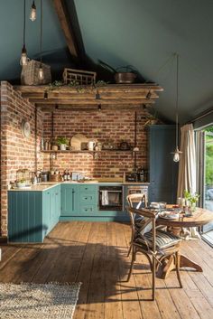 an open kitchen and dining area with brick walls, wood floors and blue painted cabinets