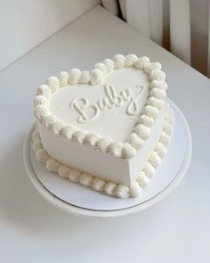 a white heart shaped cake with the word baby written on it's side sitting on a plate