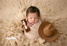 a newborn baby is holding a teddy bear and wearing a hat while laying on a blanket