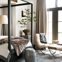 a bedroom with a four poster bed, chair and table in front of the window