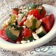 a white bowl filled with cucumber, tomato and feta cheese on top of a table