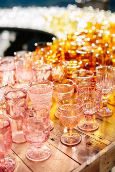 many pink glasses are lined up on a wooden table with yellow lights in the background