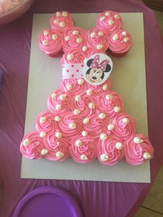 a cake shaped like minnie mouse on top of a sheet of pink frosting with cupcakes in the shape of a dress