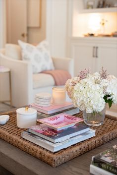 a coffee table with books, candles and flowers on it in front of a couch