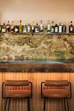 two brown leather chairs sitting in front of a bar with liquor bottles on the wall