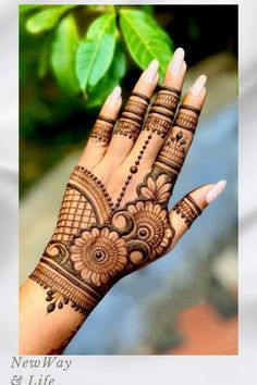 a woman's hand with henna on it and green leaves in the background