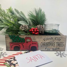 a wooden box filled with pine cones and greenery next to a sign that says fresh cut christmas trees for sale