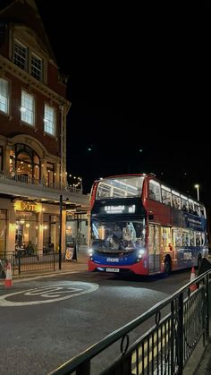 a double decker bus is driving down the street at night in front of a building