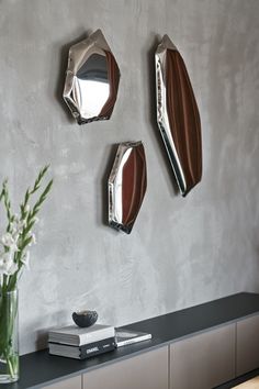 three mirrors mounted on the wall above a table with flowers in vases and books