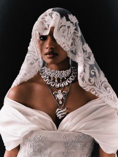 a woman in a white dress with a veil on her head and necklaces around her neck