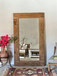 a mirror sitting on top of a wooden floor next to a vase filled with flowers