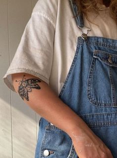 a woman wearing overalls and holding a doughnut in her right hand with a tattoo on the left arm