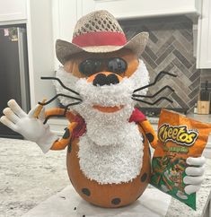 a stuffed animal wearing a hat and holding a bag of chips in his hand on top of a counter