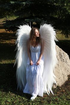 a woman dressed as an angel standing next to a rock