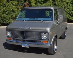 an old gray van parked in a parking lot next to some bushes and shrubbery