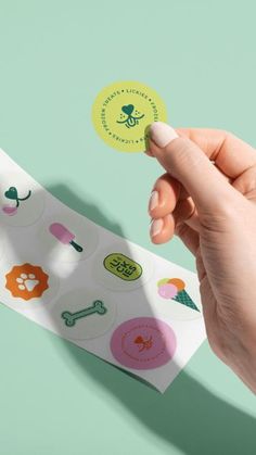 a hand holding a piece of paper with various stickers on it and a green background