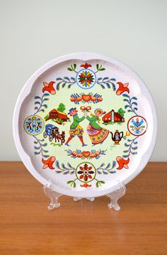 a white plate with colorful designs on it sitting on top of a wooden table next to a wall