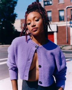 a woman with dreadlocks is standing on the street wearing a purple cardigan