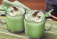 two glasses filled with green liquid and topped with whipped cream