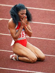 a woman kneeling down on a track with her hands clasped to her chest and eyes closed