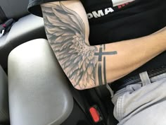 a man with a cross and wings tattoo on his arm sitting in the back seat of a car