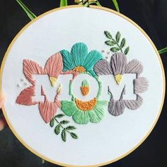 someone is holding up a hand embroidery project with the word mom spelled out in flowers