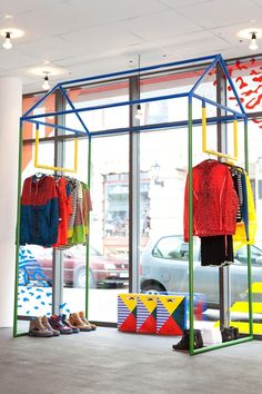 the inside of a clothing store with clothes on racks and shoes in front of it