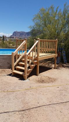 a wooden bench sitting next to a swimming pool in the middle of a dirt field