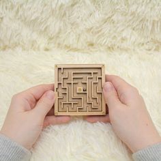 someone is holding a wooden maze board in their hands on a fluffy white surface,