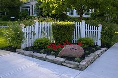 a white picket fence with red flowers in the front yard and stone rock garden bed