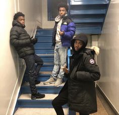 three young men standing on the stairs in front of blue staircases, one holding his hand up