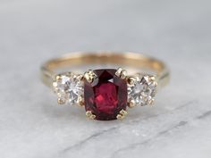 a red and white diamond ring with three stones on it's sides, sitting on a marble surface