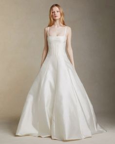 a woman in a white wedding dress standing on a gray background with her hands behind her back