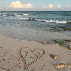 a heart drawn in the sand on a beach next to the ocean with waves coming in