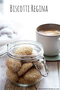 a glass jar filled with cookies next to a cup of coffee