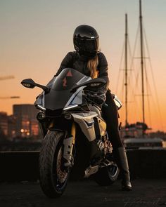 a woman sitting on top of a motorcycle in front of a city skyline at sunset