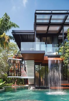 a modern house with a pool and waterfall in the front yard, surrounded by palm trees