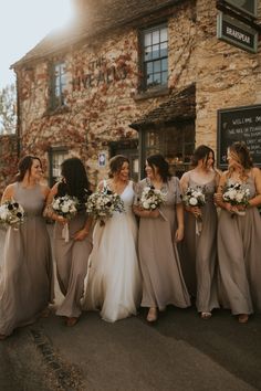 a group of women standing next to each other in front of a stone building holding bouquets