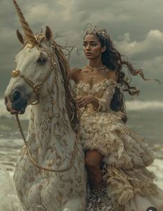 a woman riding on the back of a white horse next to the ocean in front of a cloudy sky