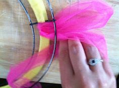 a person is holding a piece of yellow and pink tulle on a wooden surface