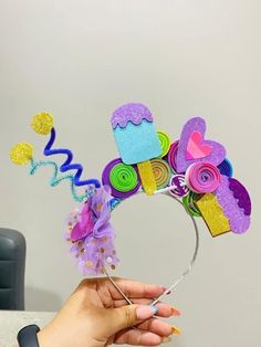 a person is holding a birthday hat made out of construction paper and colorful felts