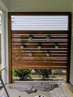 a dog laying on the ground in front of a window with potted plants hanging from it's side