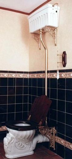 a toilet in a bathroom with black tiles and gold trim around the tank, along with a sink