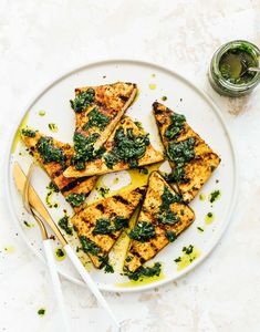 a white plate topped with slices of chicken covered in spinach next to a cup of green tea