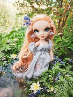 a doll is sitting in the grass with flowers around her and wearing a gray dress