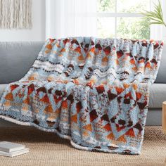 a blue and orange blanket sitting on top of a gray couch next to a window